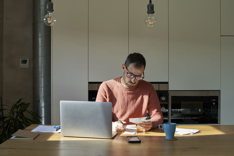 Man examining and calculating financial bills on desk at home