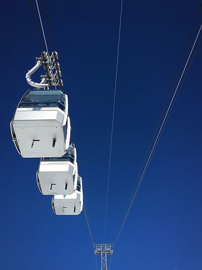 Low angle view of overhead cable cars against clear blue sky