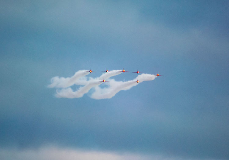 Red arrows in formation with white vapor trails in the sky performing at airshow shot from low angle