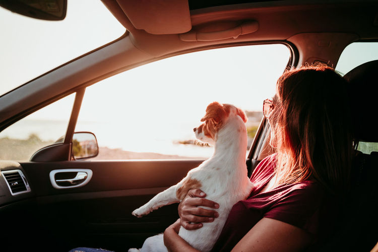 Woman sitting in car with dog during sunset