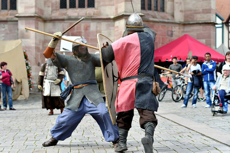 People looking at men in period costume fighting during knight tournament
