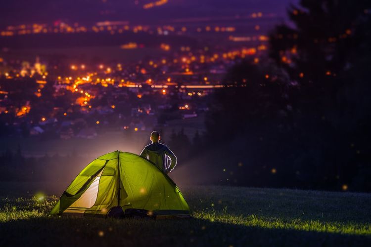 Rear view of man standing by tent at night