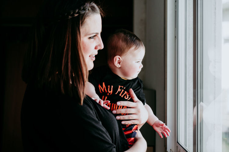 Mother and daughter embracing while standing by window at home