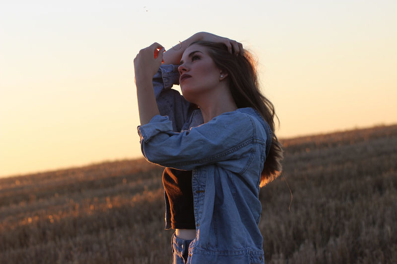 Portrait of young woman with arms raised on field during sunset