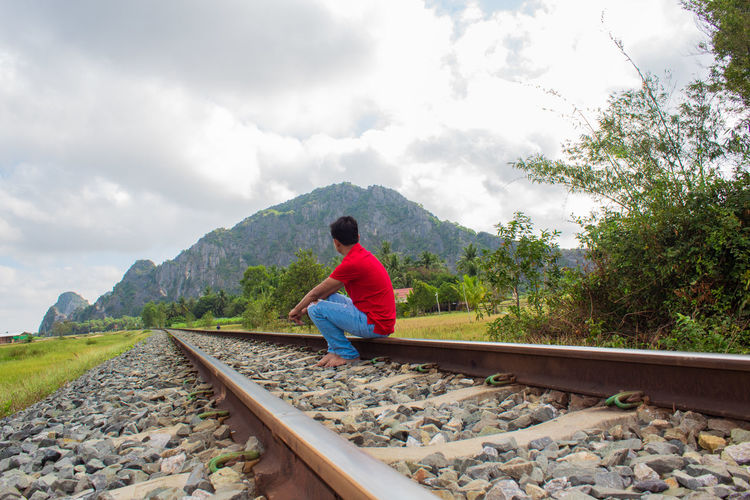 Full length of man sitting on railroad track against sky