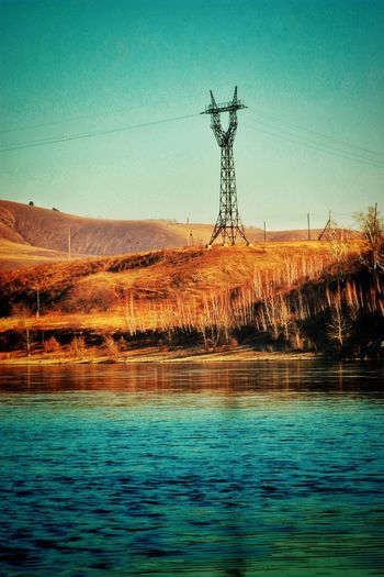 Electricity pylon by lake against sky