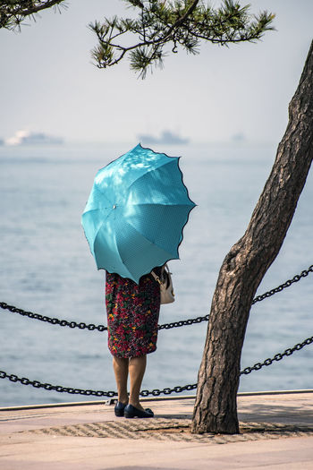 Rear view of woman with umbrella standing by sea against sky