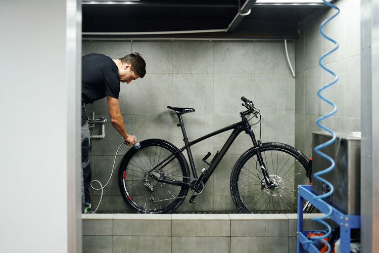 Side view of male mechanic cleaning gear cassette of bicycle wheel with water in workshop
