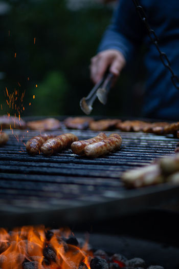 Person holding tongs with sausage on barbecue grill