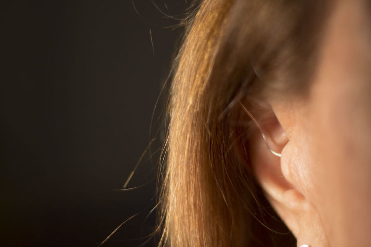 Close-up of woman wearing hearing aid against black background