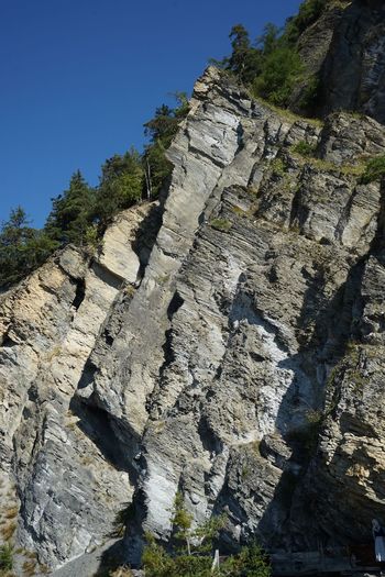 Low angle view of cliff against clear blue sky