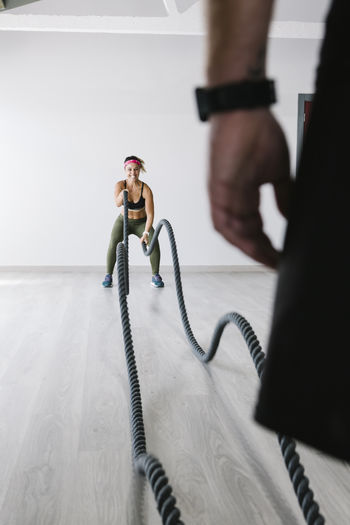 Sportive woman exercising with battle ropes at gym