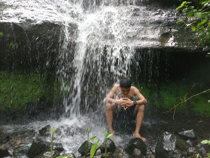 Full length of shirtless man splashing water in rocks