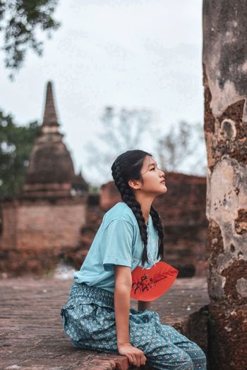 Girl looking away while sitting against temple building