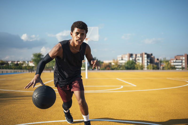 Diligent mixed race african american sportsman in uniform concentrating on dribbling ball and kicking goal on yellow playground