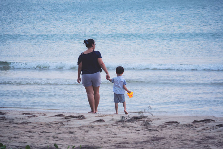 Mother and son walking on shore against sea at beach