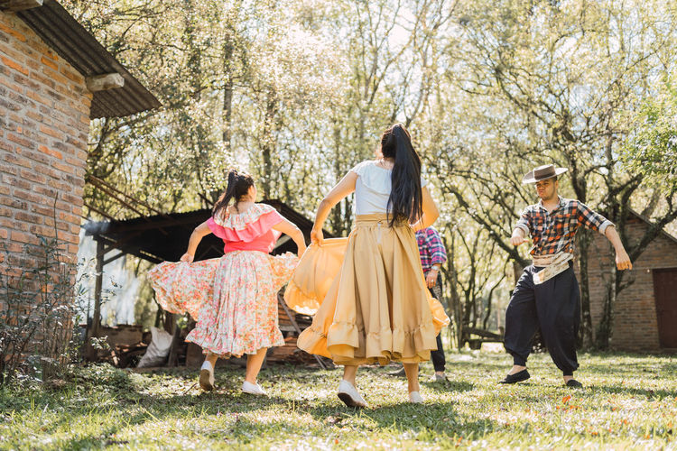 Anonymous argentinian women in traditional skirts dancing against male partners on meadow on sunny day