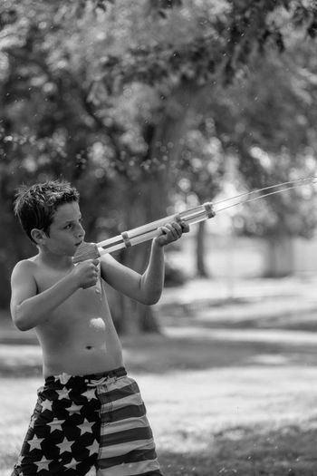 Shirtless boy spraying water with squirt gun in yard