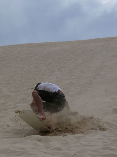 Man falling while sandboarding at desert against sky