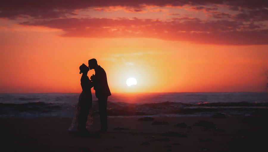 Silhouette couple standing against orange sky during sunset