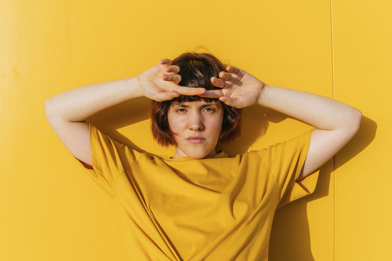 Androgynous person with arms raised standing in front of yellow wall