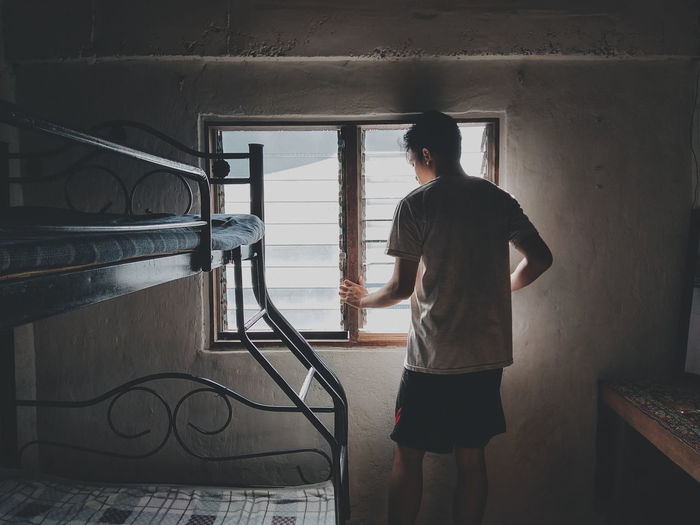 Rear view of man standing by bunkbed against window