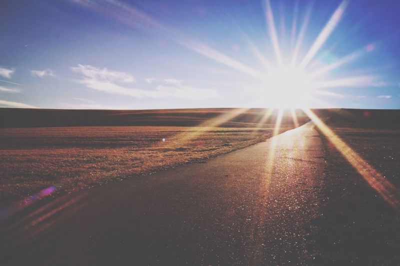 Road amidst agricultural landscape against sky during sunset