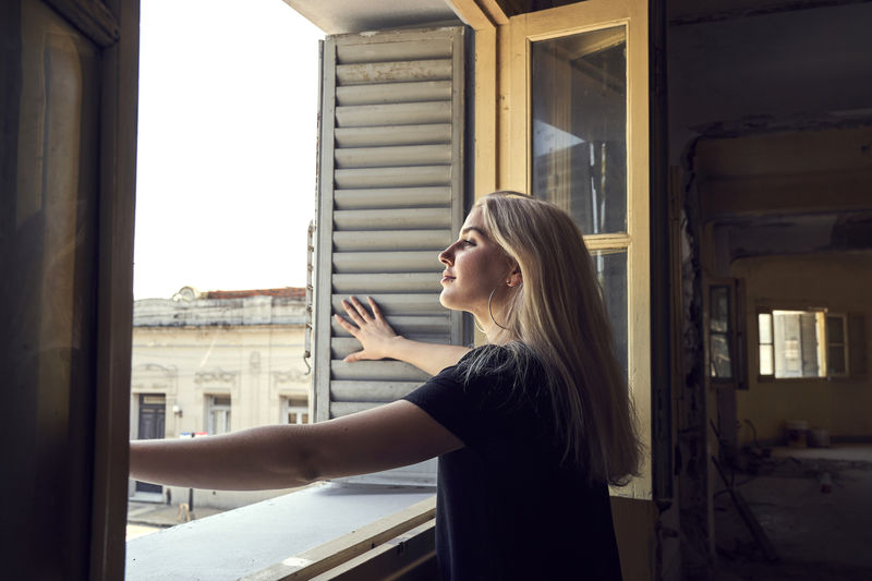Side view of woman standing against window