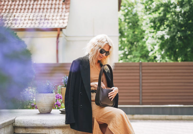 Adult elegant blonde woman in black jacket and sunglasses on summer city street