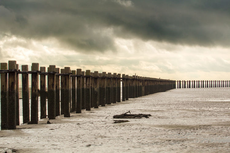 Pier on beach against cloudy sky