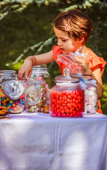 Girl taking candies from jar on table at back yard