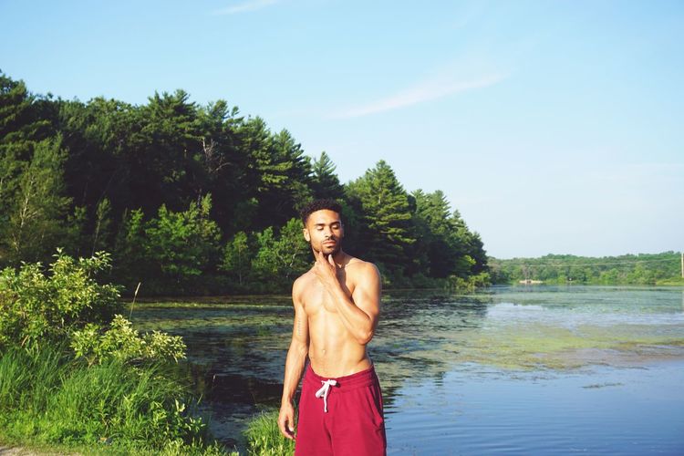 Shirtless man standing by lake