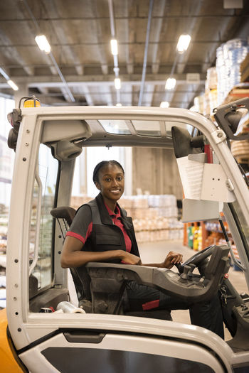 Side view of female warehouse worker sitting in forklift at warehouse