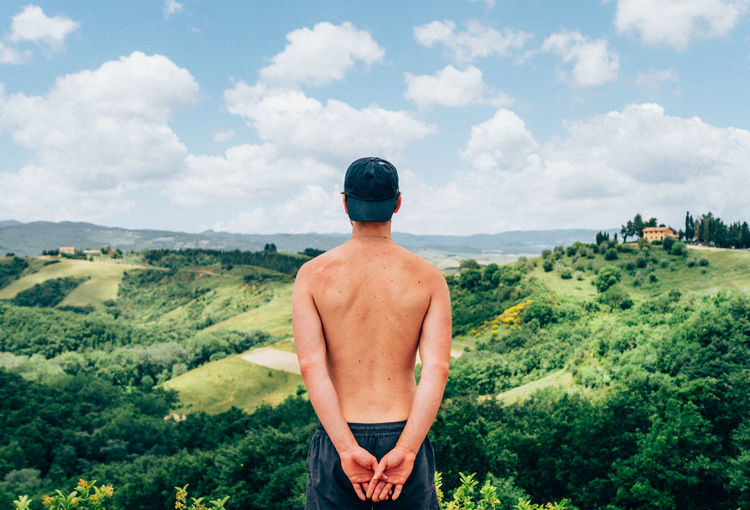 Rear view of shirtless man looking at green landscape