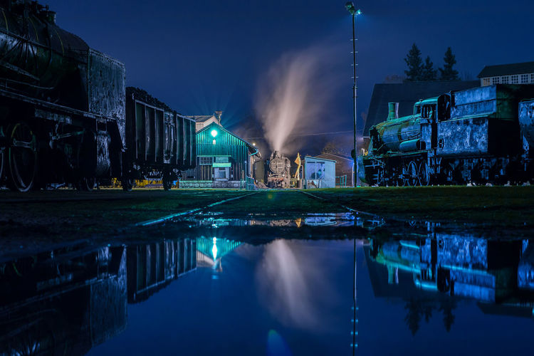 Illuminated buildings by lake against sky at night