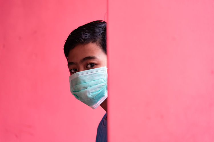 Portrait of young man against pink background with face mask