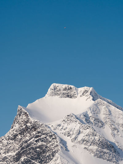 Low angle view of snowcapped mountain and helicopter against clear blue sky 