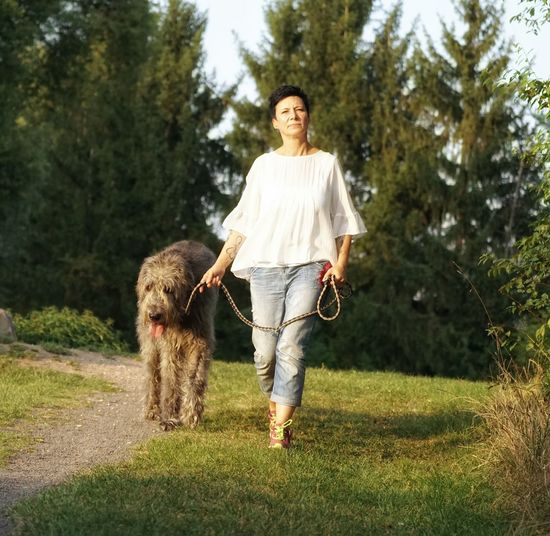 Woman with irish wolfhound walking on field against trees