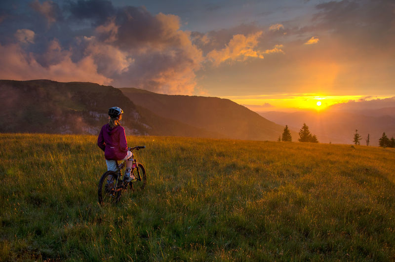 Woman with bicycle on field against sky during sunset