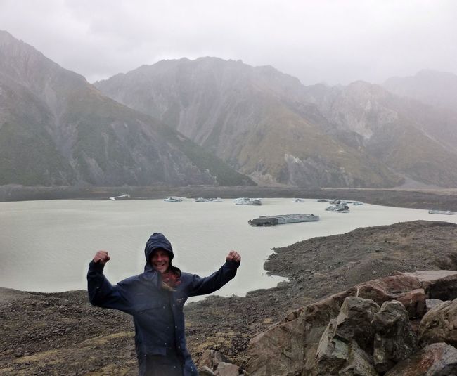 Portrait of happy hiker flexing muscle against lake and mountains during foggy weather