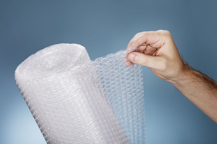 Close-up of person hand holding bubble wrap against blue sky