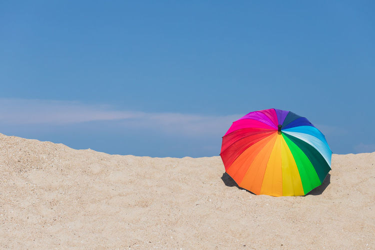 Multi colored umbrella on beach against blue sky