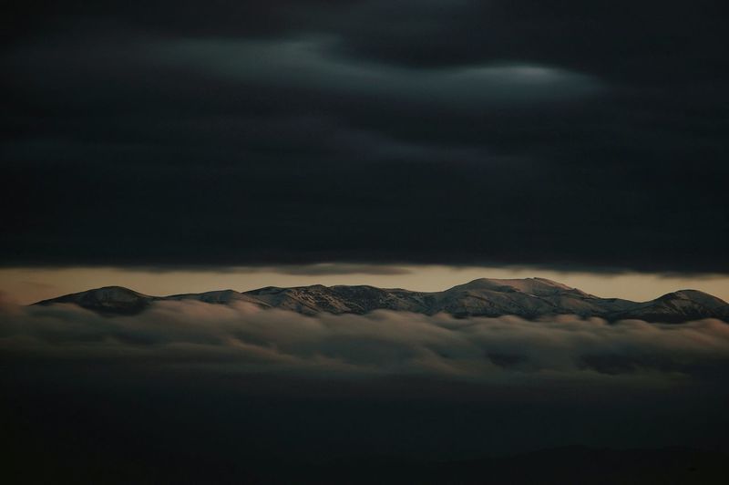 Scenic view of clouds covering snowcapped mountains during sunset