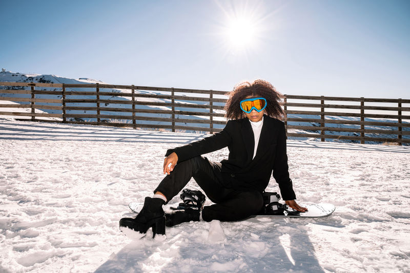 African american woman with goggles and a snowboard on a snowy mountain during winter