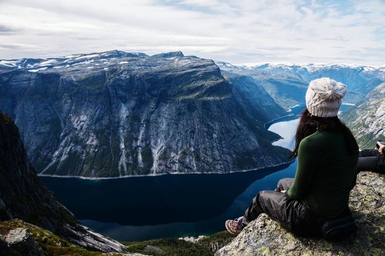 Woman sitting on cliff against valley