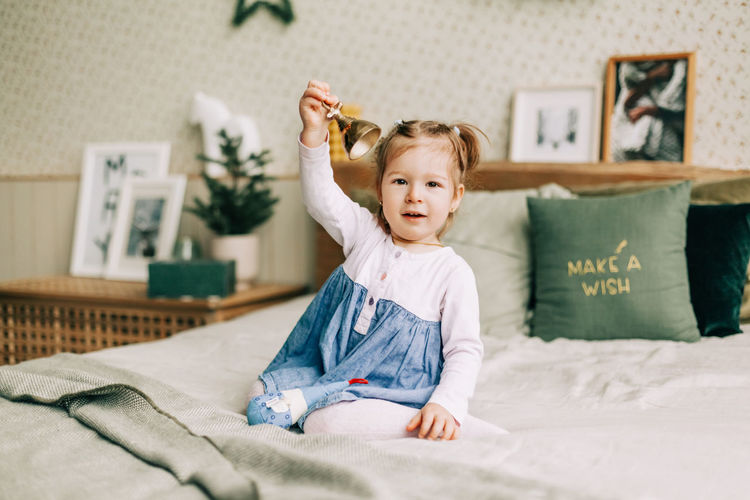 A happy girl is playing on the bed on christmas morning in a room decorated for christmas