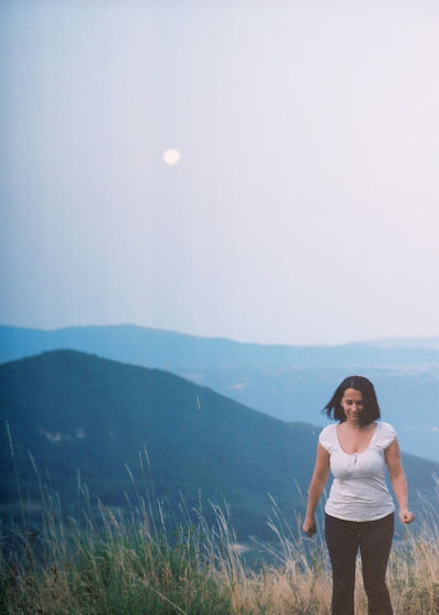 Woman standing with the mountains and the moon in the background at dawn