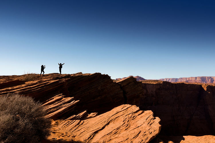 Low angle view of people standing on desert against clear blue sky
