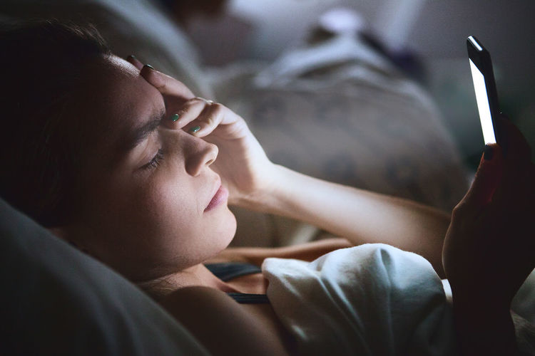 Close-up of woman with mobile phone in bed