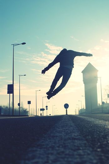 Rear view full length of man jumping over road against sky